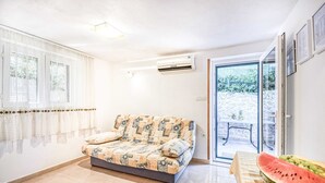 A living room with a sofa, a table with a watermelon and grapes, and a sliding glass door leading to an outdoor area.