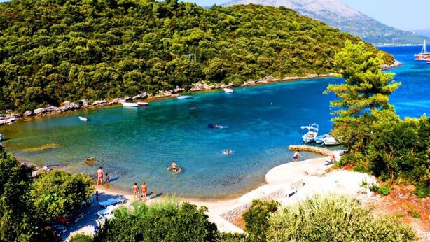 Una zona costera con aguas turquesas cristalinas, una playa de arena y colinas verdes exuberantes al fondo.