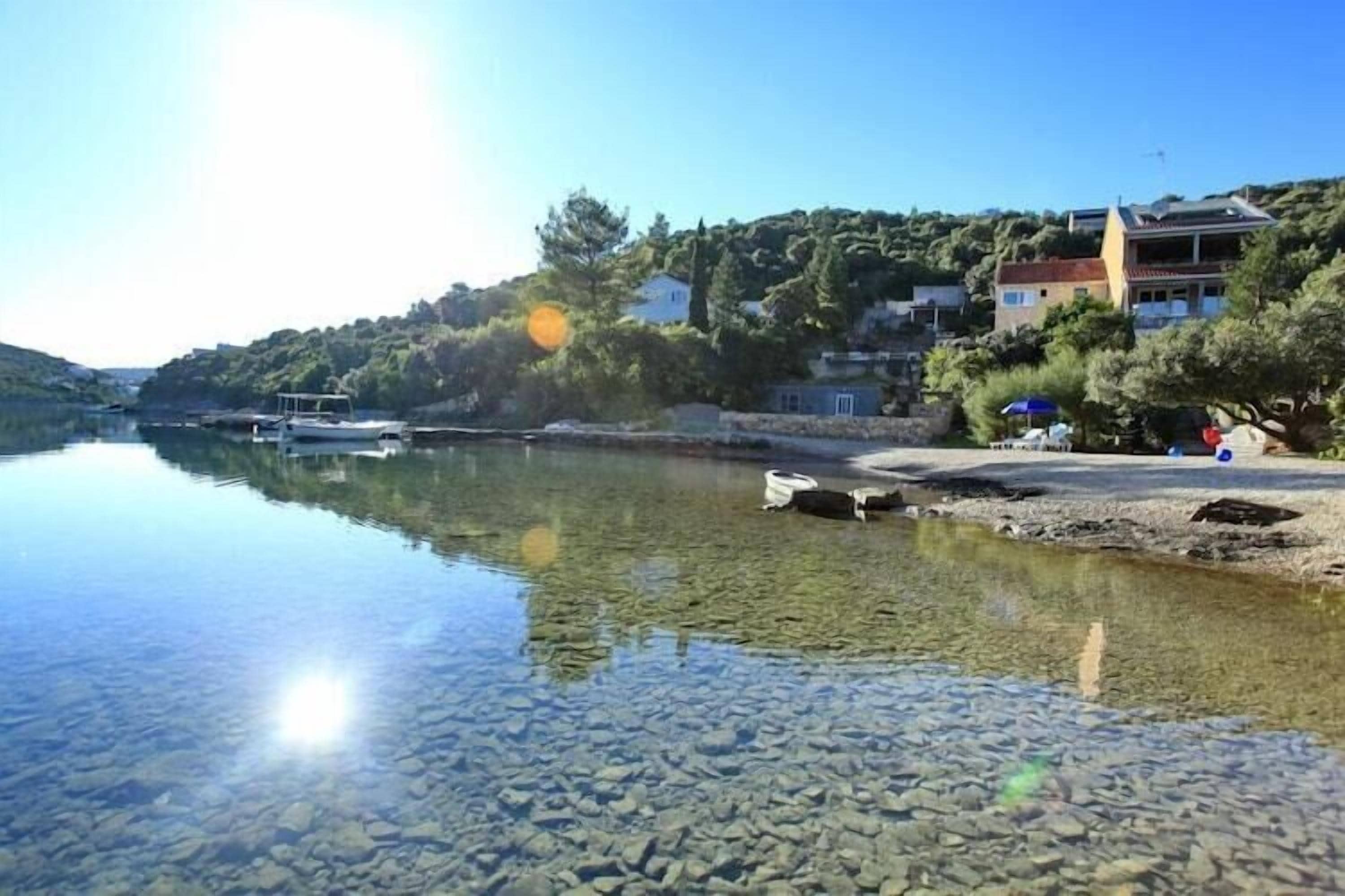A clear lake with boats, a beach, and buildings on a hillside.