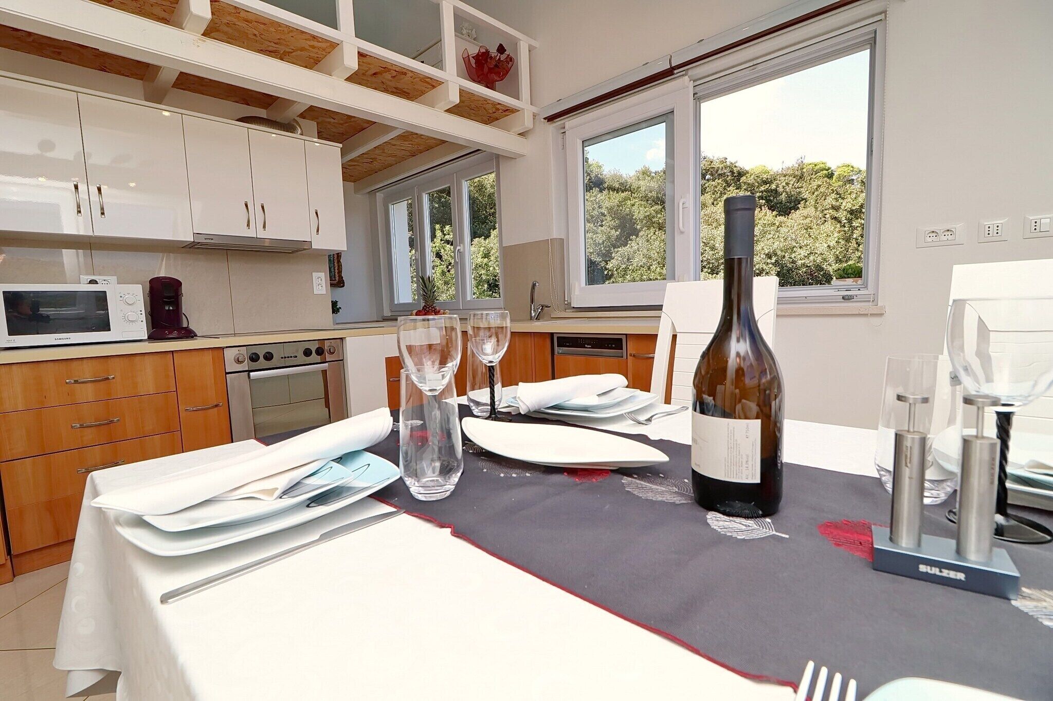 A modern kitchen with white cabinets, a microwave, a coffee maker, and a dining table set for two with wine glasses and a bottle.