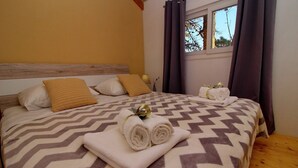 Una cama bien hecha con un edredón estampado, dos toallas enrolladas y una almohada decorativa.