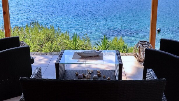 Una terraza con mobiliario de mimbre, una mesa de vidrio y vistas al mar.