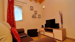 Una sala de estar con sofá, reposapiés, televisor y una mesita con un bol de aperitivos.