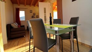 Un comedor con mesa y sillas de vidrio, una botella de vino y vistas al exterior.