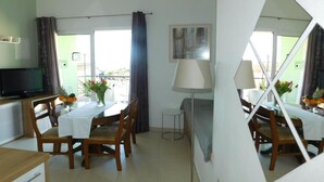 A dining area with a table set for four, a television on a stand, and a window with curtains.