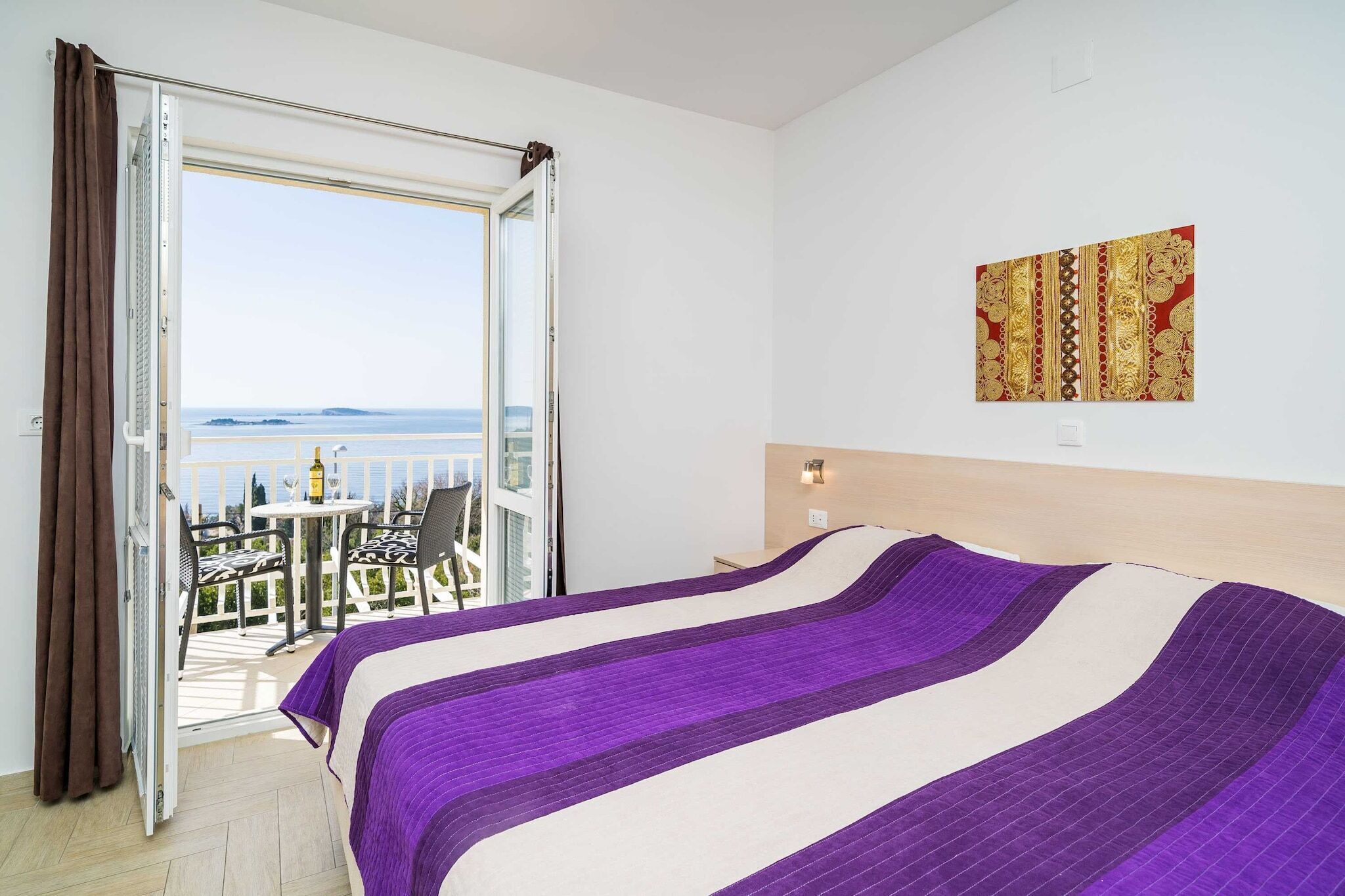 A hotel room with a bed, a balcony with a table and chairs, and a view of the sea.