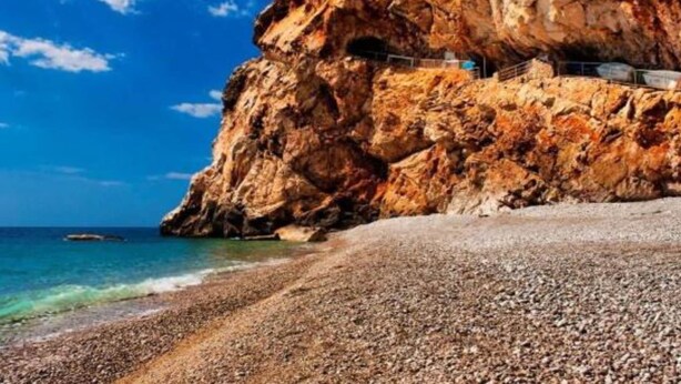A rocky cliff with a pebble beach and a clear blue sky.