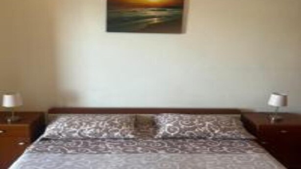 Un dormitorio con una cama, dos mesitas de noche, un cuadro colgado en la pared y una colcha estampada.