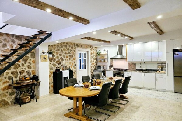 A spacious kitchen with white cabinets, a dining area with a wooden table, and a stone wall.