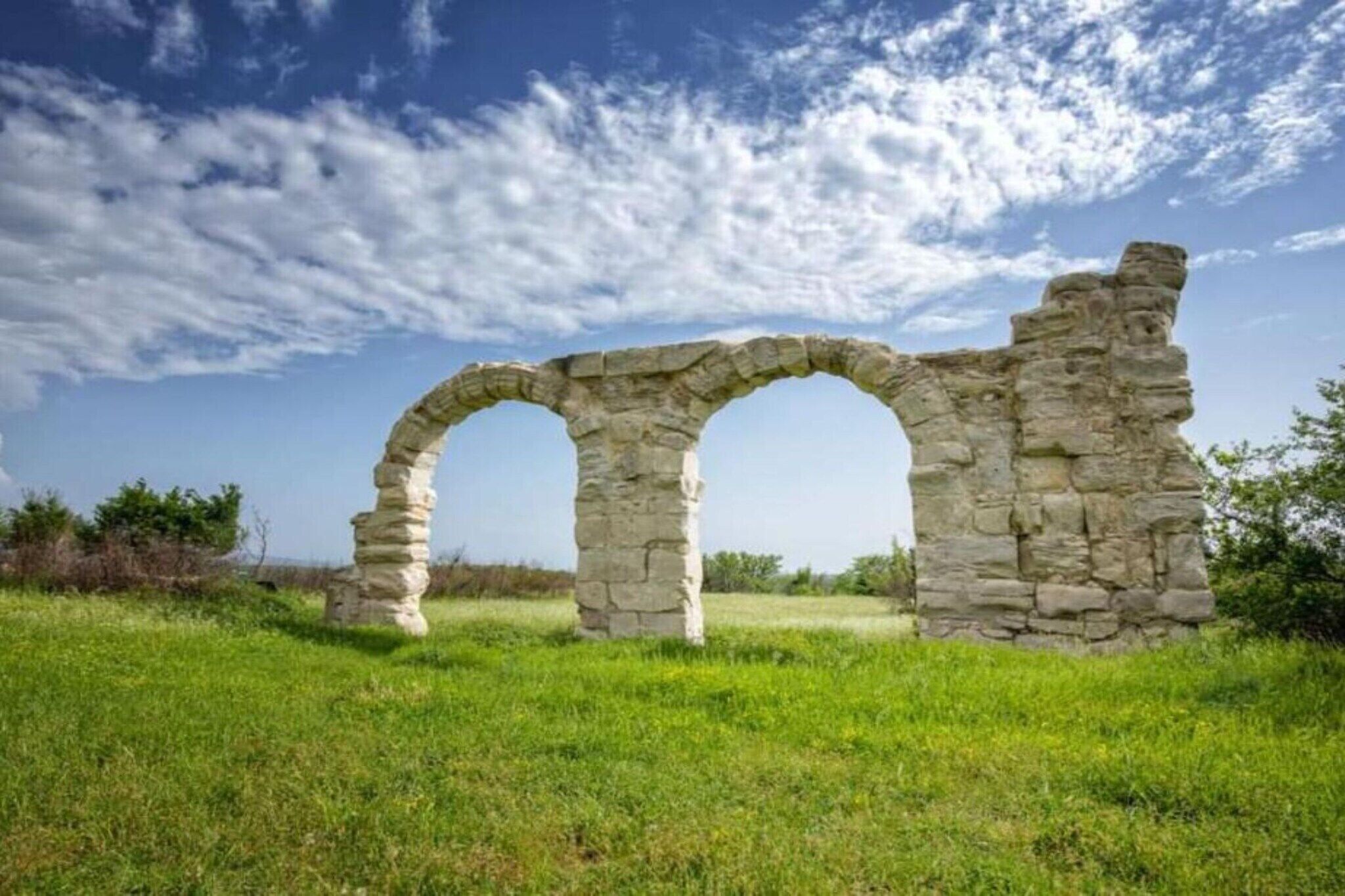 Ein steinernes Bogenportal in einem grasbewachsenen Feld unter blauem Himmel.