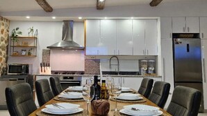 A modern kitchen with white cabinets, a stainless steel refrigerator, and a dining area with a long table set for six. - Villa Nika - Three Bedroom Villa with Private Pool (Lozovac)