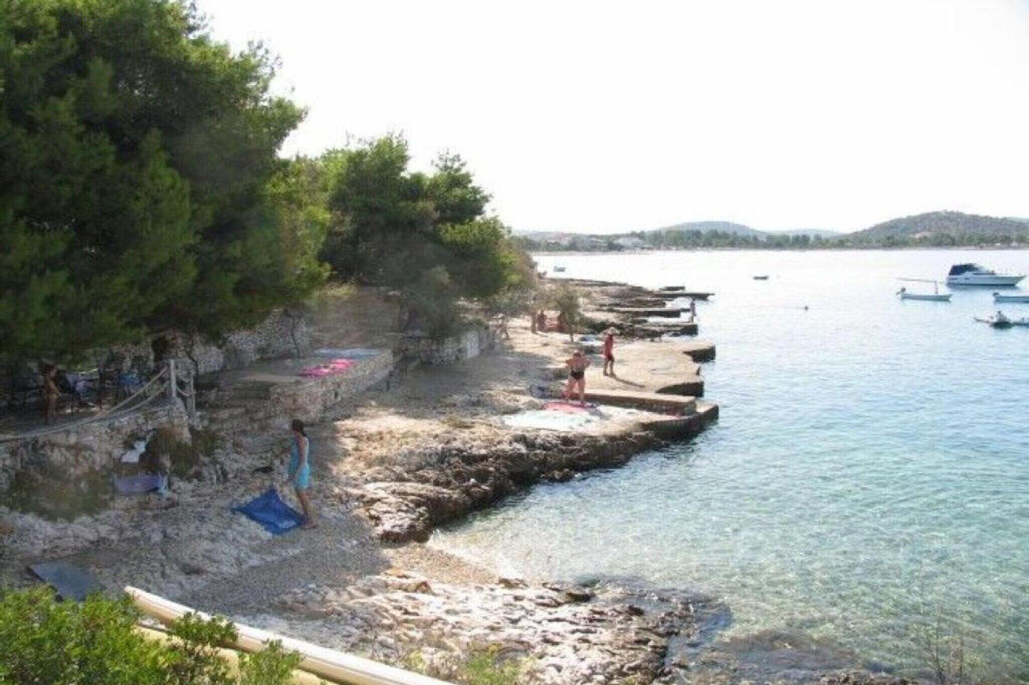 Ein felsiger Strand mit klarem Wasser, Booten und Bäumen.