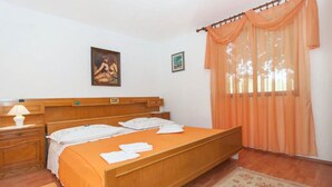 Een slaapkamer met een houten bed, een nachtkastje met een lamp, een bloemenkleed en een raam met oranje gordijnen.