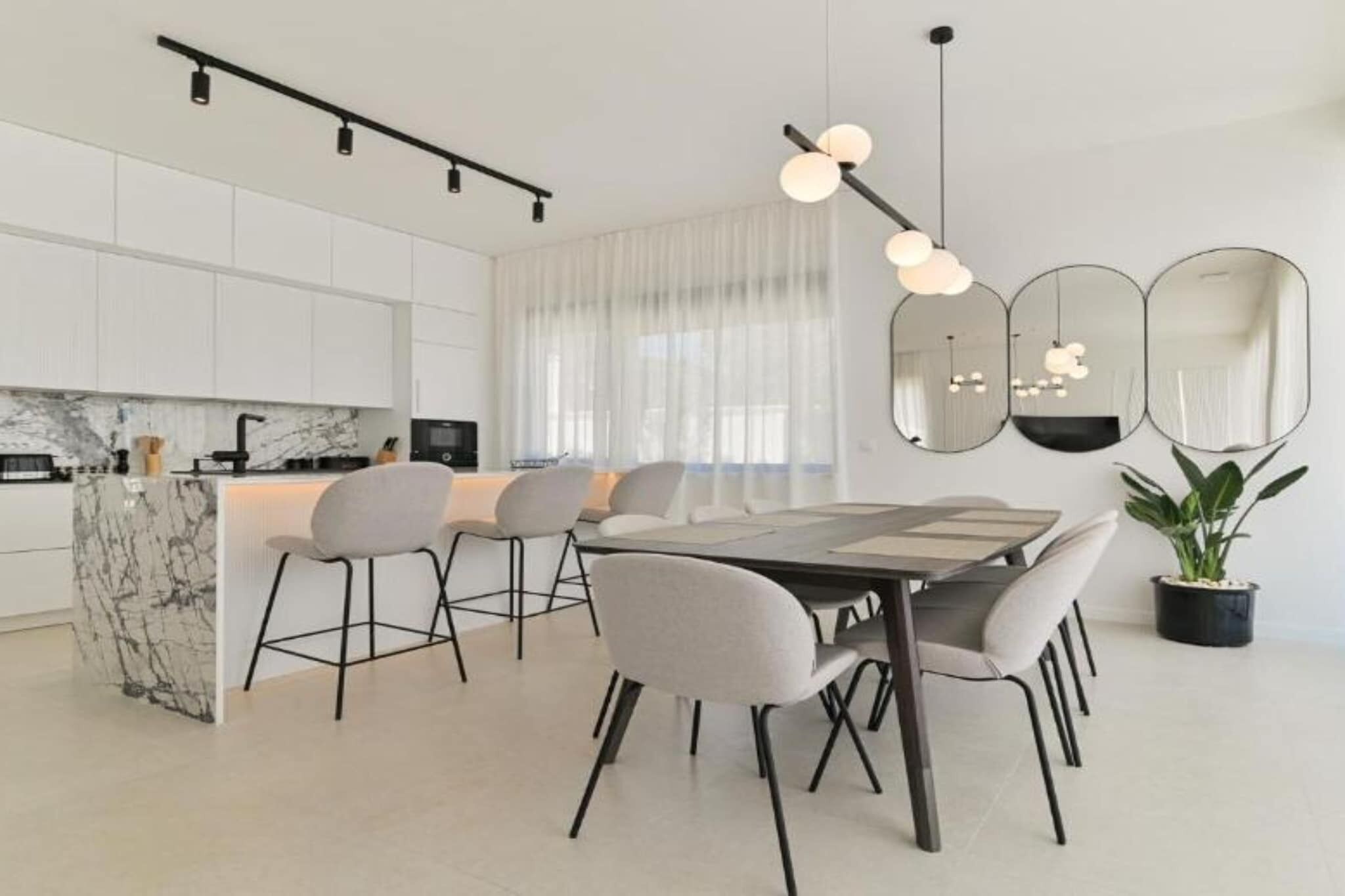 A modern kitchen with white cabinets, a marble island, and a dining area with a table and chairs.