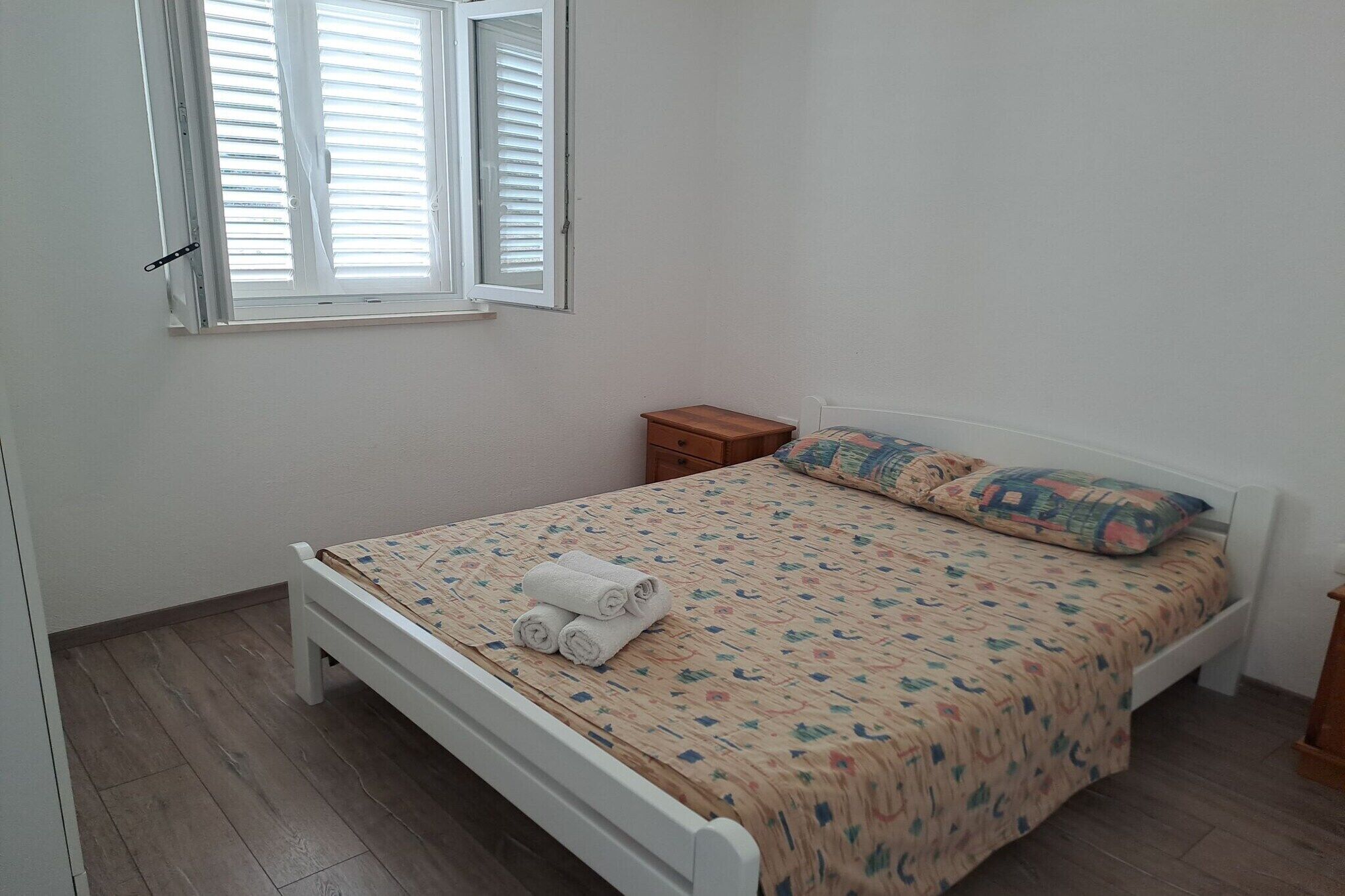 Ein Schlafzimmer mit einem Einzelbett, einem Nachttisch, einem Fenster mit Jalousien und Holzboden.