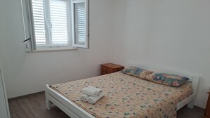 Ein Schlafzimmer mit einem Einzelbett, einem Nachttisch, einem Fenster mit Jalousien und Holzboden.