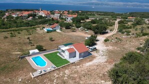 Ein Luftbild eines Küstengrundstücks mit Swimmingpool, einem freistehenden Haus und einer Straße, die zu einem Dorf führt.
