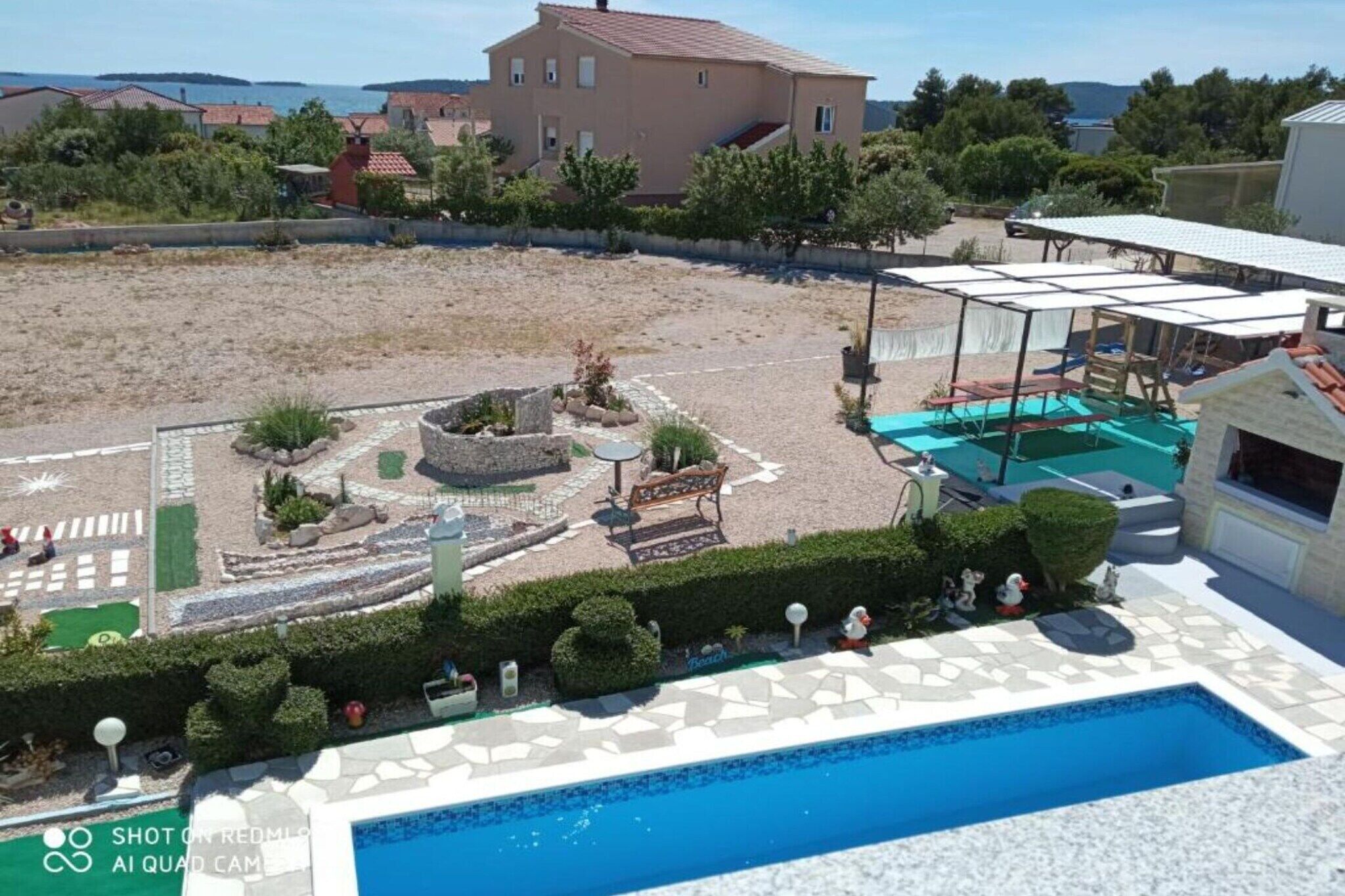 A swimming pool with a sunshade, a patio area with a bench, and a landscaped garden with a small fountain.