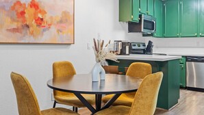 Een moderne keuken met groene kasten, een roestvrijstalen koelkast en een eethoek met een ronde tafel en gele stoelen.