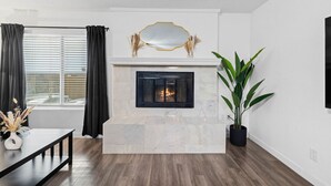 Een moderne woonkamer met een open haard, een eethoek met een zwarte tafel, en een grote potplant.