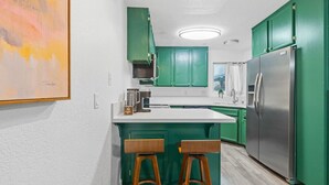 Een keuken met groene kastjes, een roestvrijstalen koelkast en een wit aanrecht.