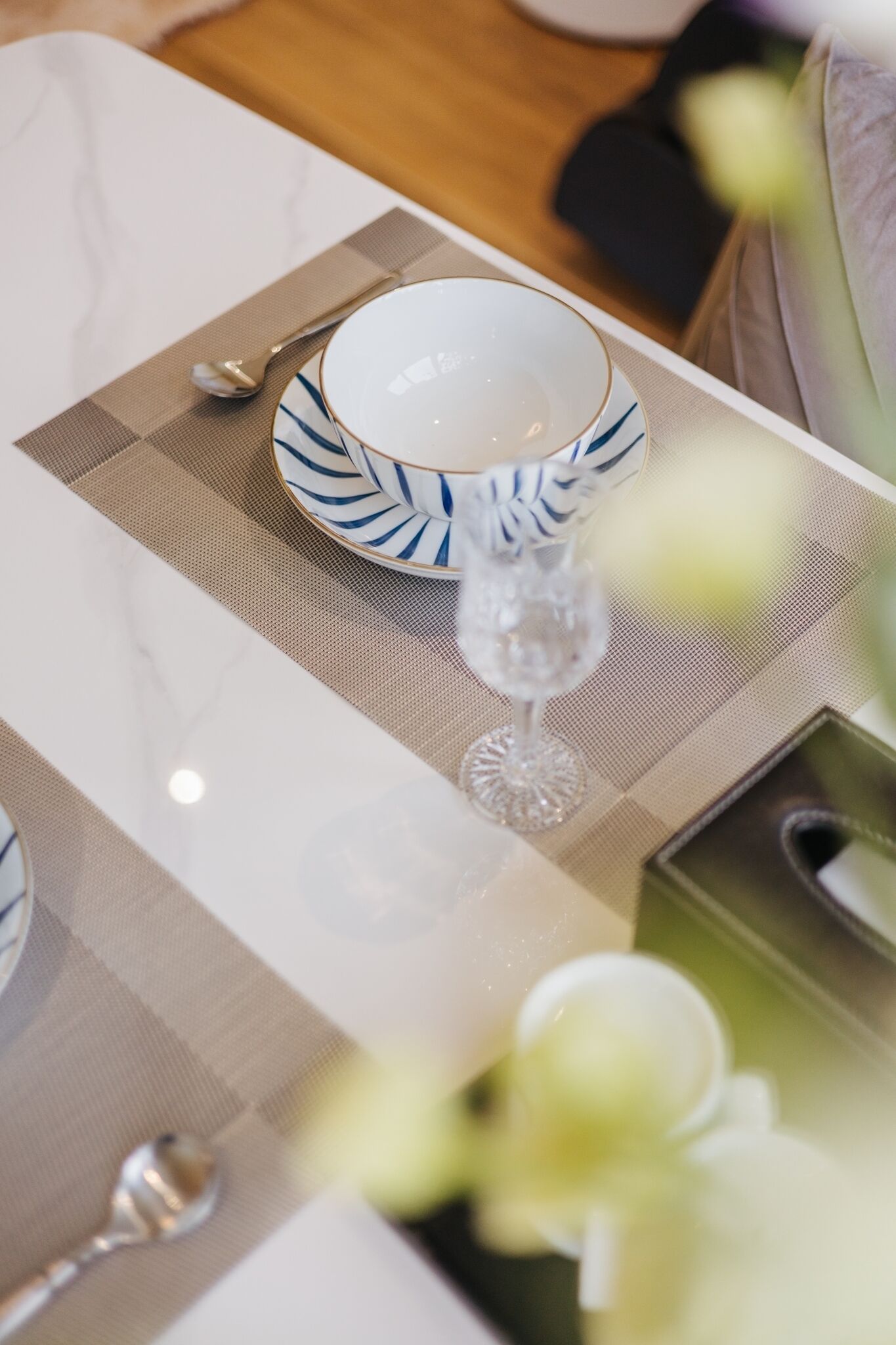 A table set with a white plate, a blue and white patterned bowl, a clear glass, and a spoon on a beige placemat.