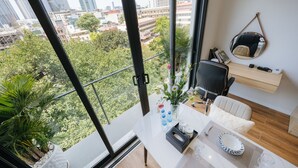 Una camera moderna con un'ampia finestra che si affaccia su una vista urbana, una scrivania con una sedia, uno scaffale piccolo e uno specchio.