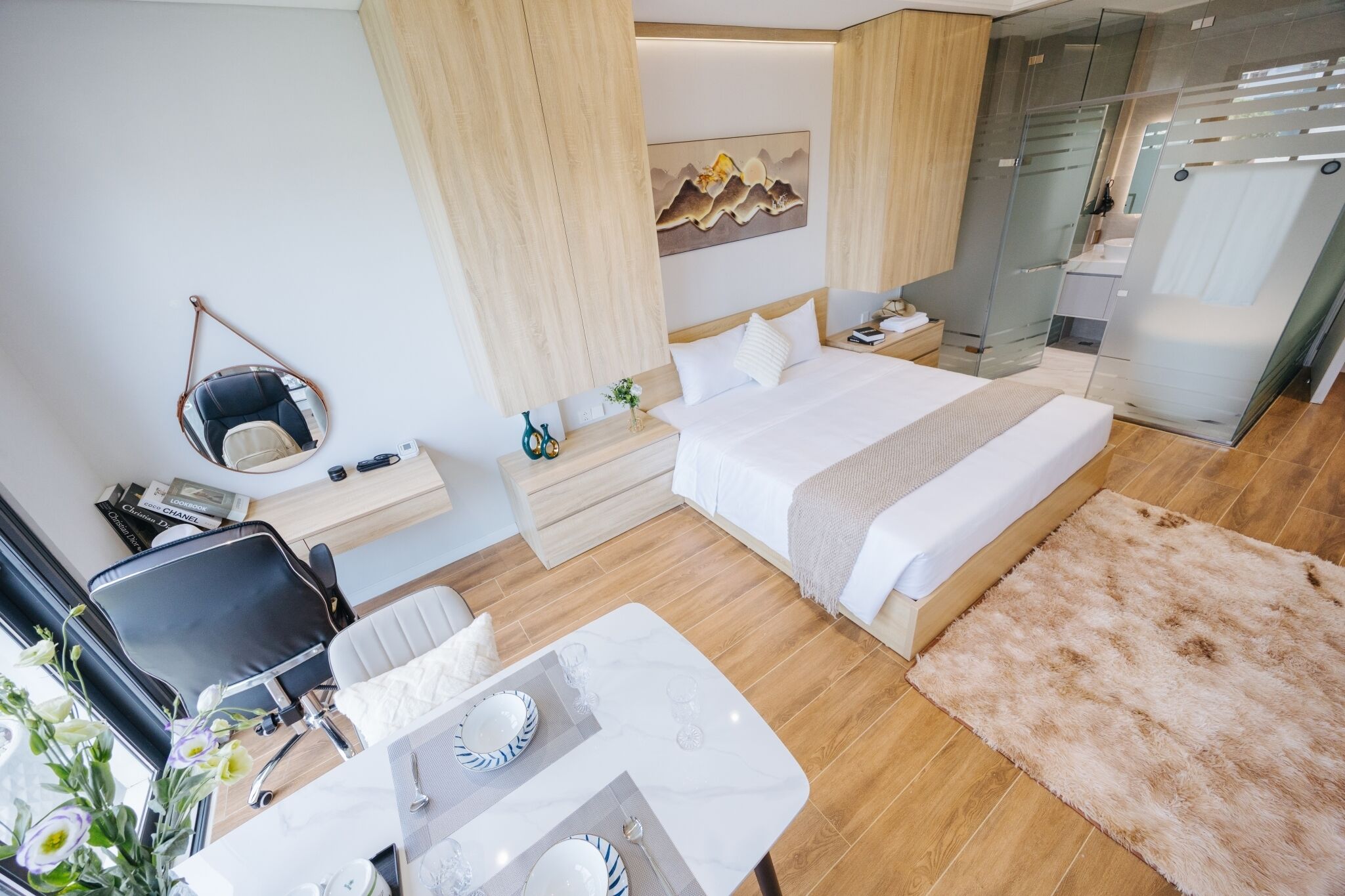 A modern hotel room with a large bed, a desk with a chair, a small table, and a mirror.