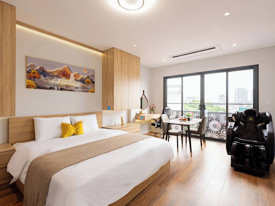 Quarto de hotel moderno com uma cama grande, uma mesa de escritório, uma cadeira de massagem e vista para a cidade através de amplas janelas.