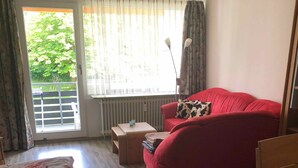 A room with a bed, a red sofa, a wooden chair, a small table, and a radiator. - Beautiful vacation apartment on the edge of the Swabian Alb, hiking, relaxing, thermal baths! (Beuren)