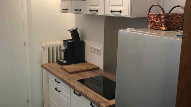A compact kitchen with white cabinets, a built-in stove, a refrigerator, and a wicker basket on top. - Beautiful vacation apartment on the edge of the Swabian Alb, hiking, relaxing, thermal baths! (Beuren)