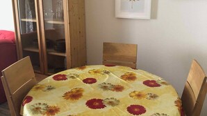 A dining area with a round table covered by a floral tablecloth, surrounded by wooden chairs. A wooden cabinet with glass doors is to the left, and there are two framed pictures on the wall. - Beautiful vacation apartment on the edge of the Swabian Alb, hiking, relaxing, thermal baths! (Beuren)