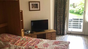 A bedroom with a bed, a TV, a wooden wardrobe, a desk with a chair, and a window with curtains. - Beautiful vacation apartment on the edge of the Swabian Alb, hiking, relaxing, thermal baths! (Beuren)