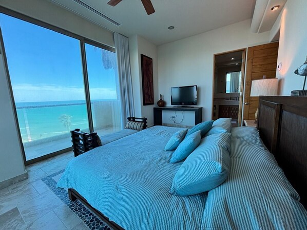 Quarto com cama grande, televisão e vista para o mar.