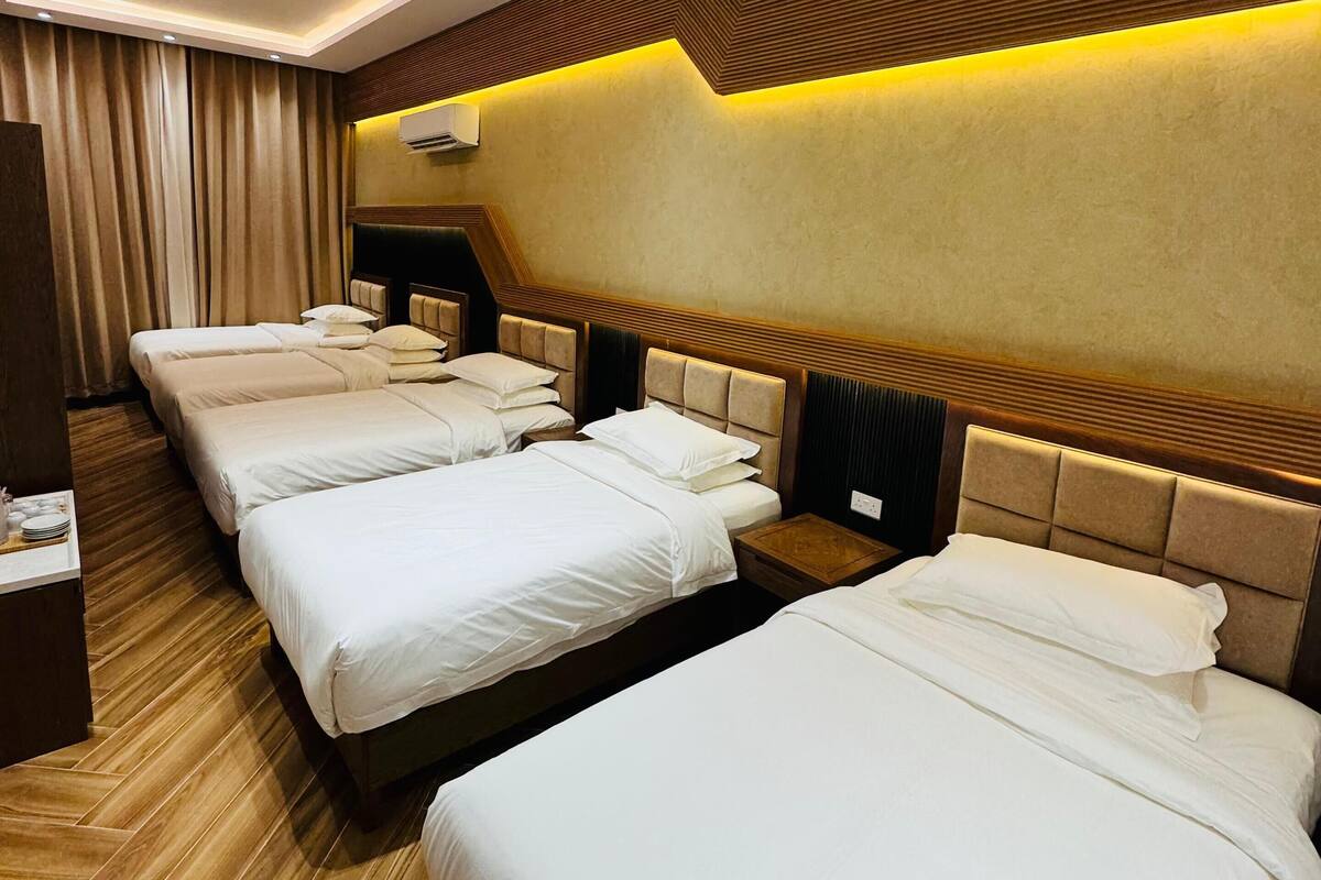 A hotel room with four beds arranged in a row, wooden flooring, and a modern design with a wooden headboard and wall paneling.
