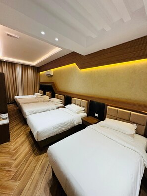 Habitación de hotel con cuatro camas dispuestas en fila, suelo de madera y diseño moderno que incluye un cabecero y paneles de madera.