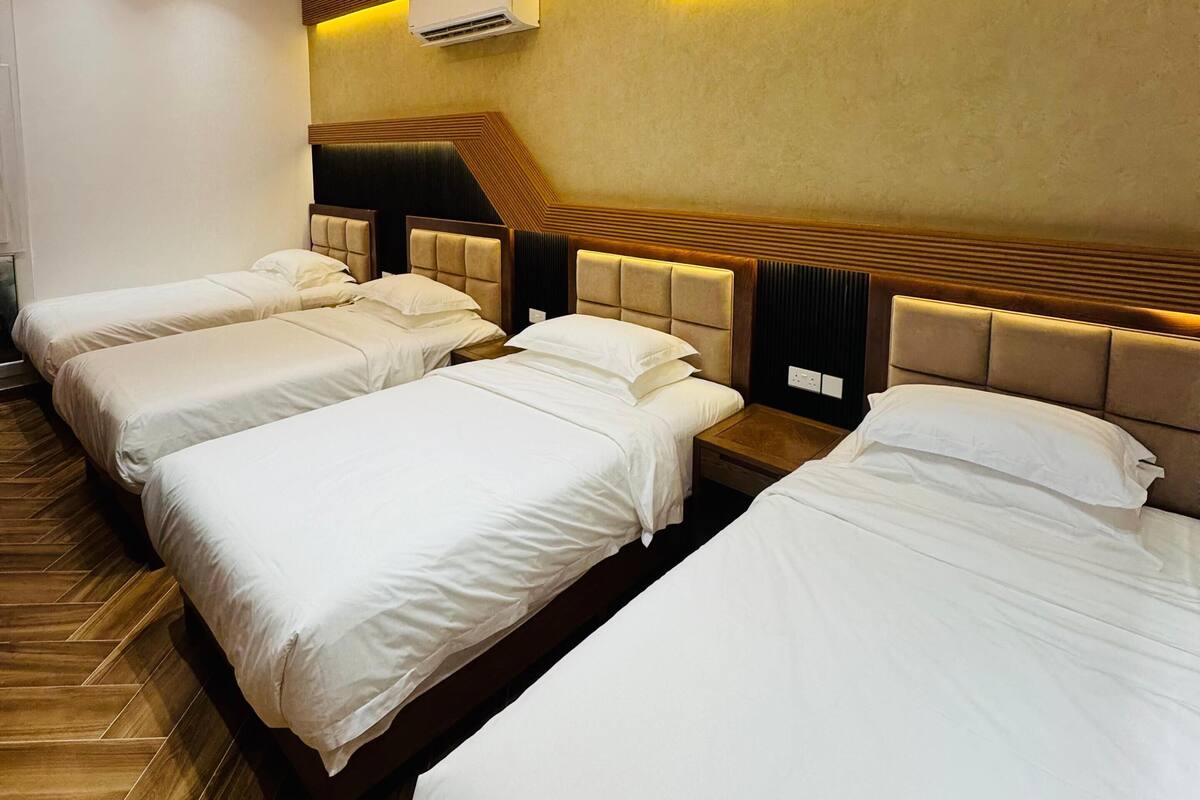 A hotel room with three beds, wooden paneling on the walls, recessed ceiling lights, and an air conditioning unit.