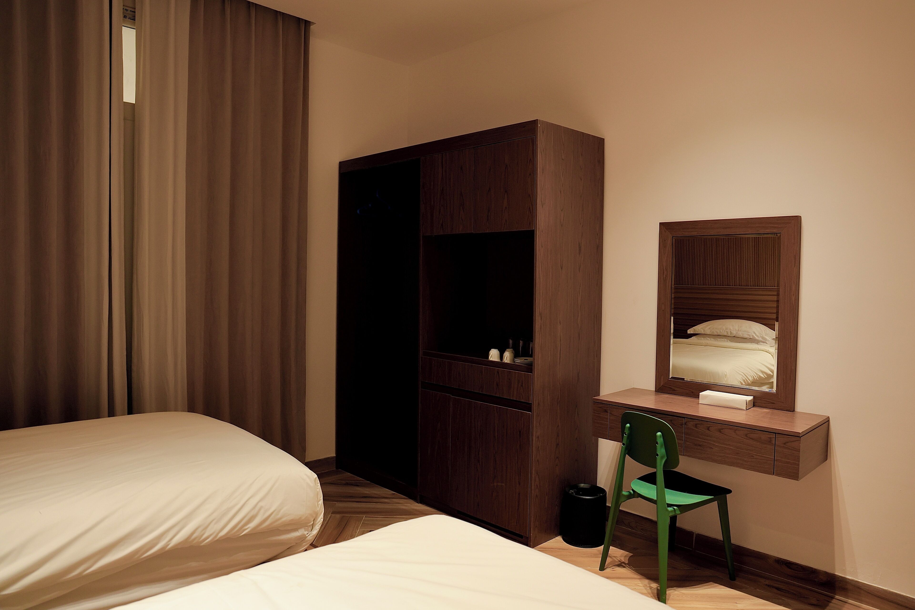 A hotel room with a bed, a desk with a chair, a wardrobe, and a mirror.