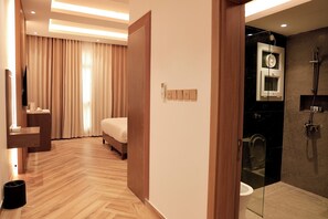 Una habitación de hotel moderna con suelo de madera, una cama, una tocador con espejo y un baño con cabina de ducha de vidrio.