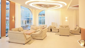 A spacious living area with multiple sofas and a coffee table, large windows offering a view of the outdoors, and a modern ceiling design with circular lighting. - Dreamland Resort Salalah (Salalah)