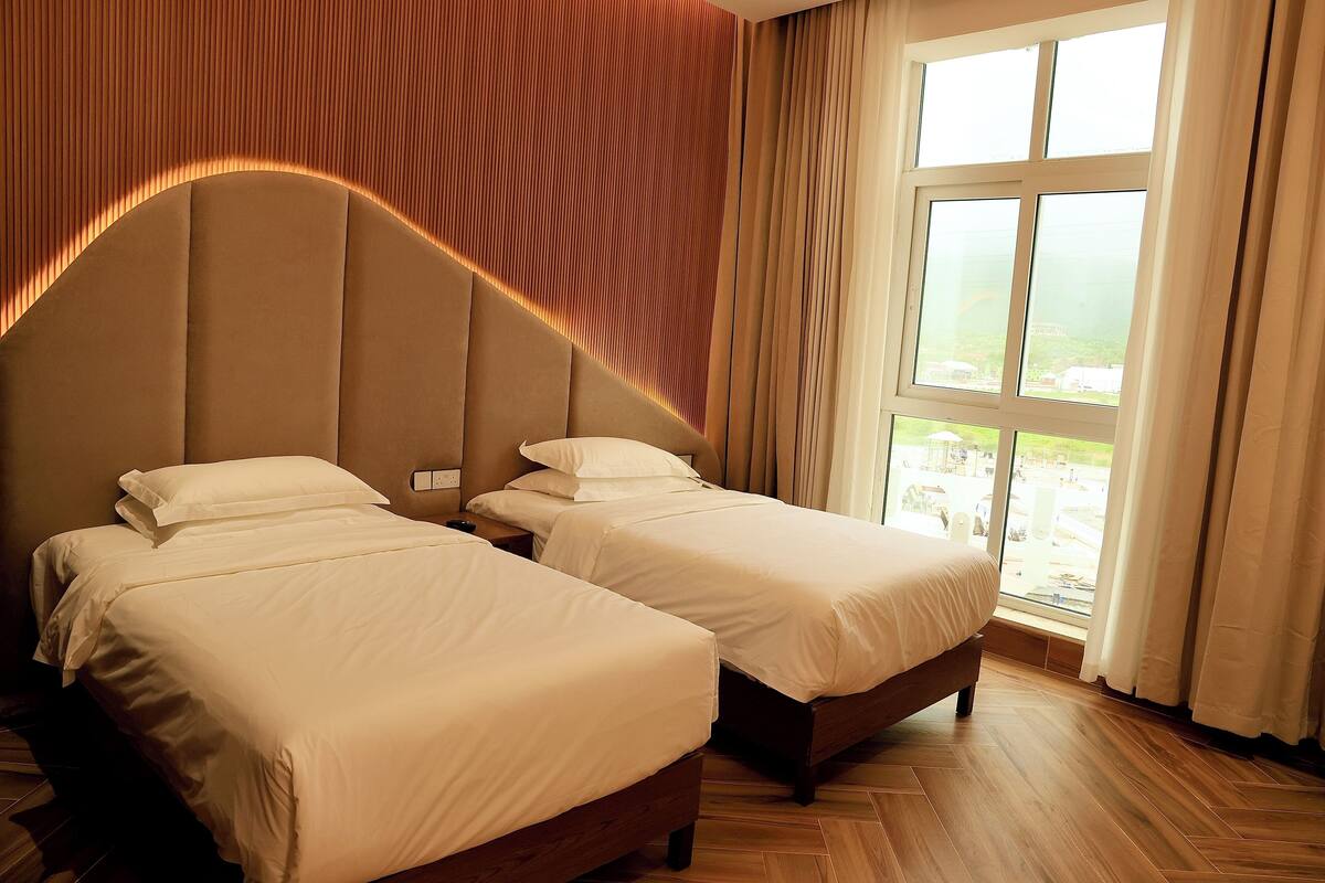 A hotel room with two beds, a large window with curtains, and a wooden floor.