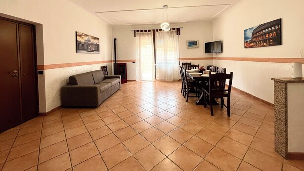 A living room with a sofa, a dining table with chairs, a fireplace, and a television on the wall. - Sun & Sea 2 steps from Rome (Fiumicino)