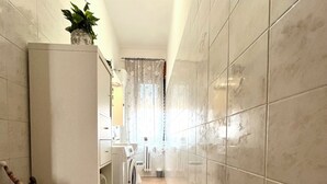 A narrow hallway with tiled walls and floor, leading to a laundry area with a washing machine and dryer. - Sun & Sea 2 steps from Rome (Fiumicino)