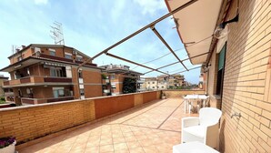 A rooftop terrace with tiled flooring, white wicker furniture, and a brick wall. - Sun & Sea 2 steps from Rome (Fiumicino)