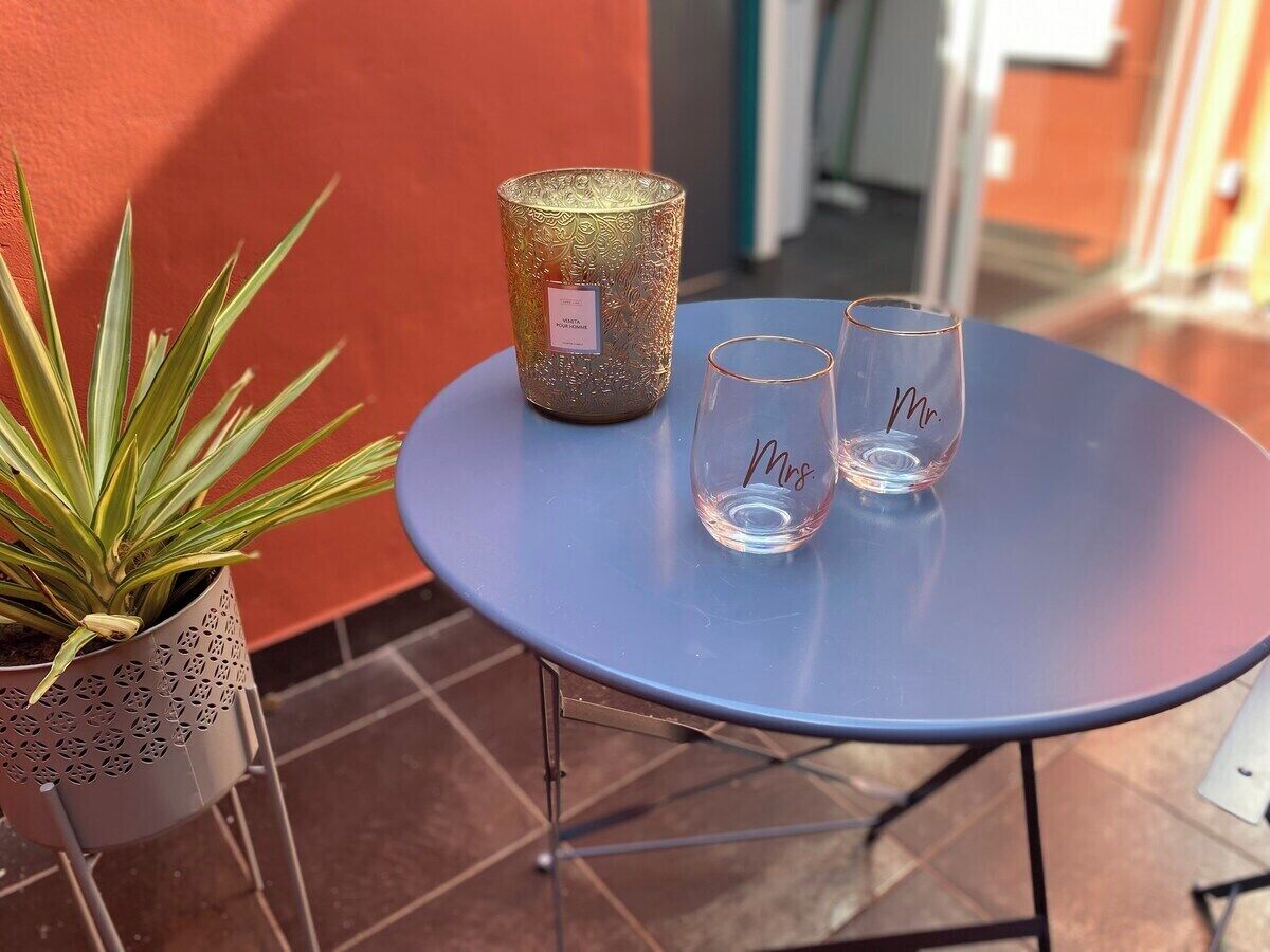 Ett litet runt bord med en blå duk, två genomskinliga glas och en dekorativ ljusstake.
