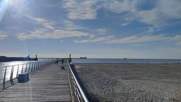 Eine Holzstege, der sich in einen Strand erstreckt, mit blauem Himmel und ruhiger See.