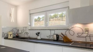 Een moderne keuken met een groot raam, witte kasten en een minimalistische inrichting.