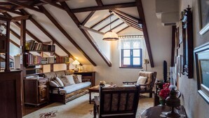 Una sala de estar acogedora con techo alto, vigas de madera, un sofá, un sillón, una mesita y una estantería llena de libros.