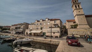 Un pueblo histórico con edificios de piedra, una torre destacada y un puerto deportivo con barcos.