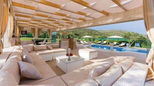 A spacious outdoor seating area with a pool and a scenic view of hills.
